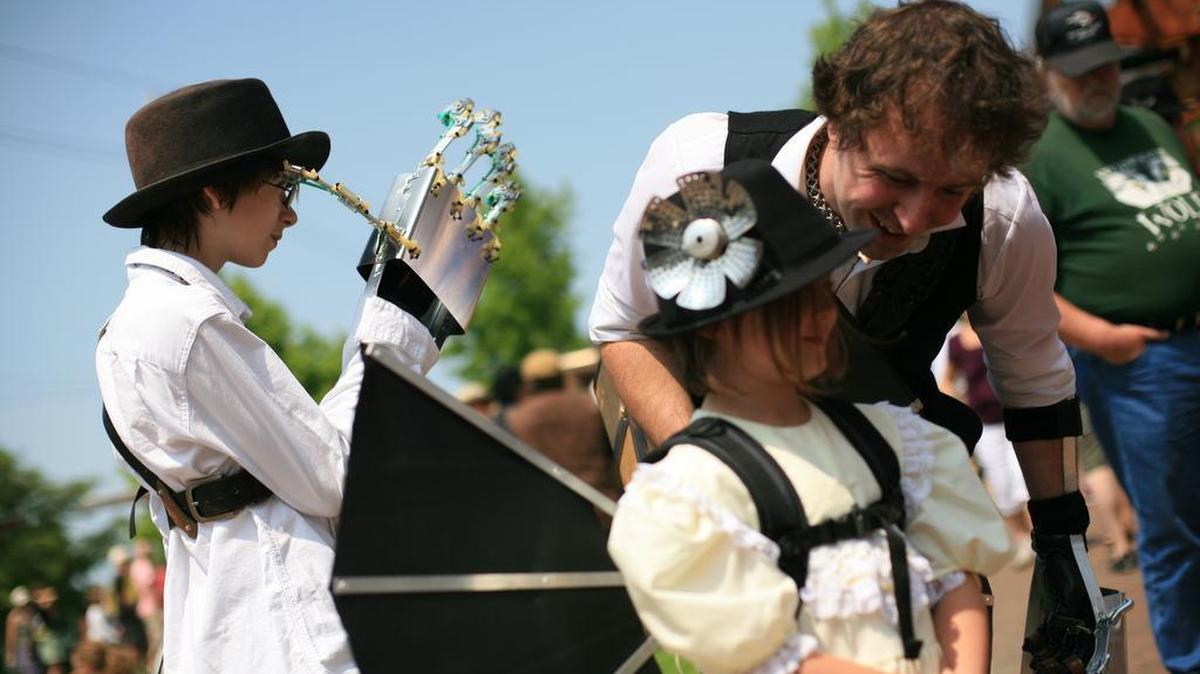 Elijah Forslof, left, uses a mechanical hand to push his hair back from his face as his stepfather and sister wait in line for a balloon at the Fairhaven Steampunk Festival in 2012.