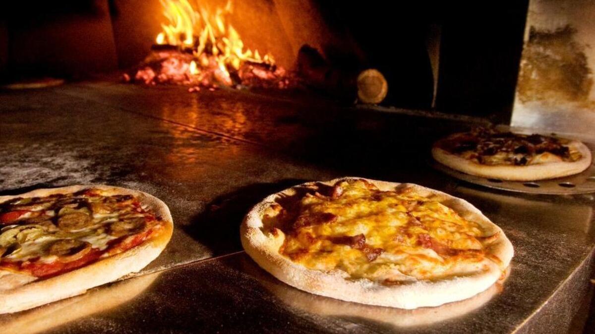 Three pizzas sit on the edge of the wood-burning oven at La Fiamma Wood Fire Pizza in downtown Bellingham.