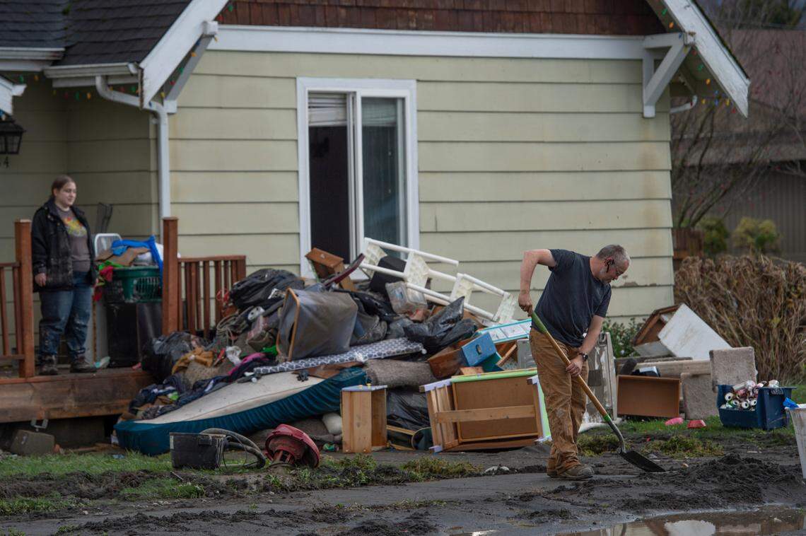 Dean Lambert scrapes mud from the sidewalk in front of his home Friday, Nov. 19, after severe flooding earlier in the week in Sumas.