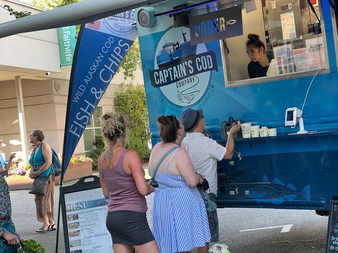 Customers order food at the Captain’s Cod food truck during the Commercial Street Block Party in downtown Bellingham on Thursday, July 28. Meals at the food truck serving clam chowder and fish and chips are packaged in hard paper containers in compliance with a new city ordinance aimed at curbing waste from single-use plastic.