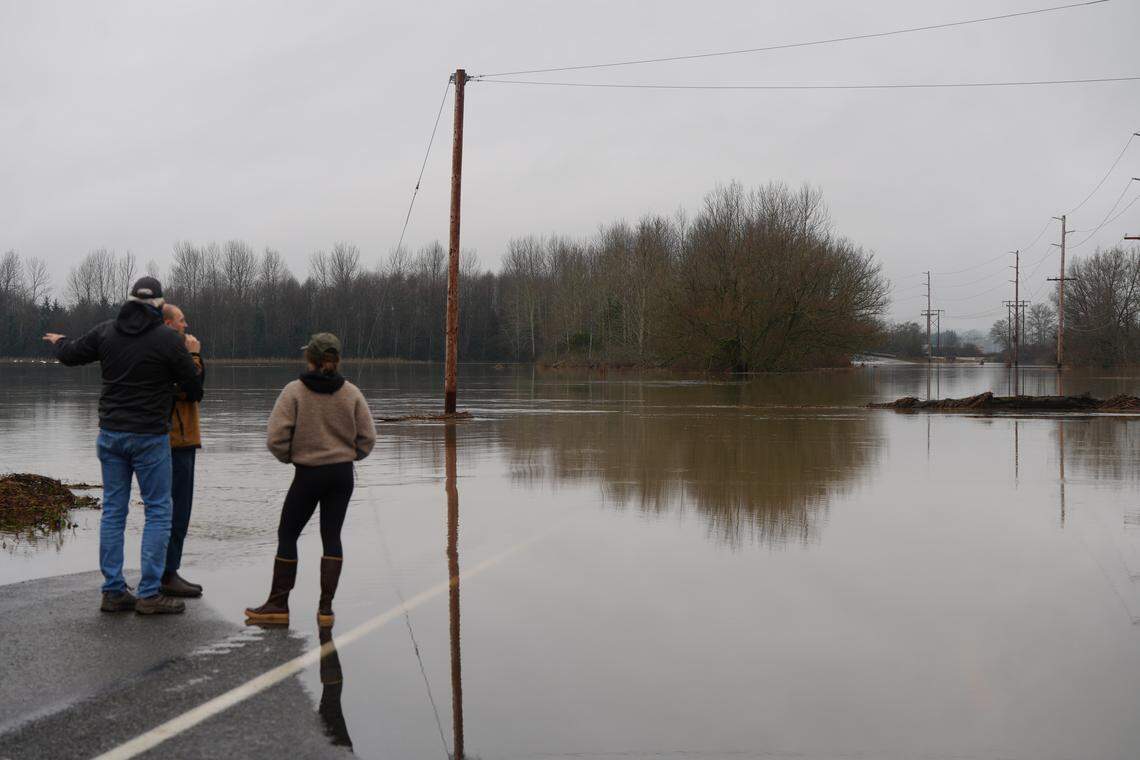 Community members look out across floodwaters over Slater Road on Dec. 12 in Bellingham after the Nooksack River overflowed its banks, blocking access to Lummi Nation.