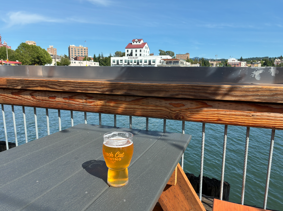 A glass of Beach Cat Brewing’s Smash Cat IPA is pictured, with the downtown Bellingham waterfront in the background.