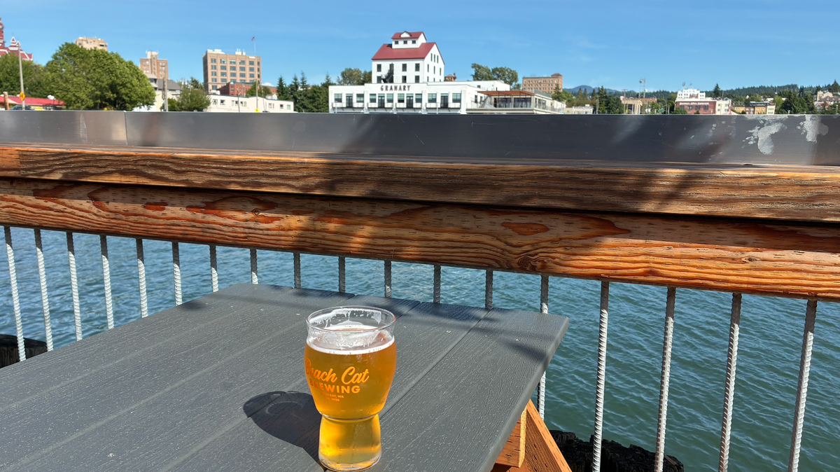 A glass of Beach Cat Brewing’s Smash Cat India pale ale sits on a table at the bewery, with the downtown Bellingham waterfront in the background.