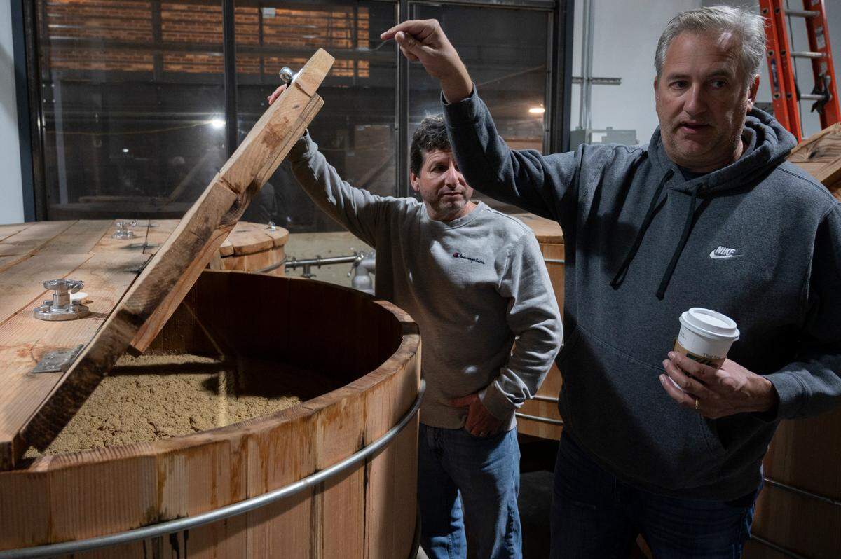 Co-owners Kelly Andrews, right, and Ethan Lynette of Chuckanut Bay Distillery show fermenting grain inside a wooden barrel at their distillery on Thursday, April 28, in Bellingham.
