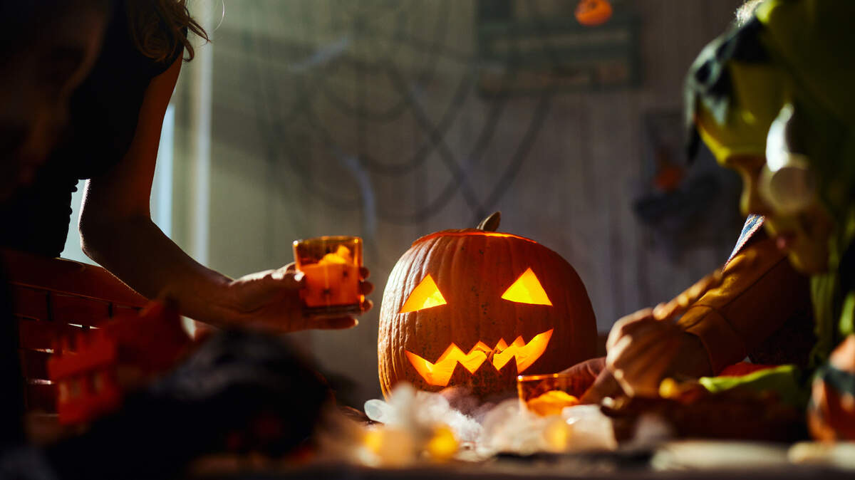 Close up of Jack O’ Lantern on dining table with unrecognizable people arranging it on Halloween.