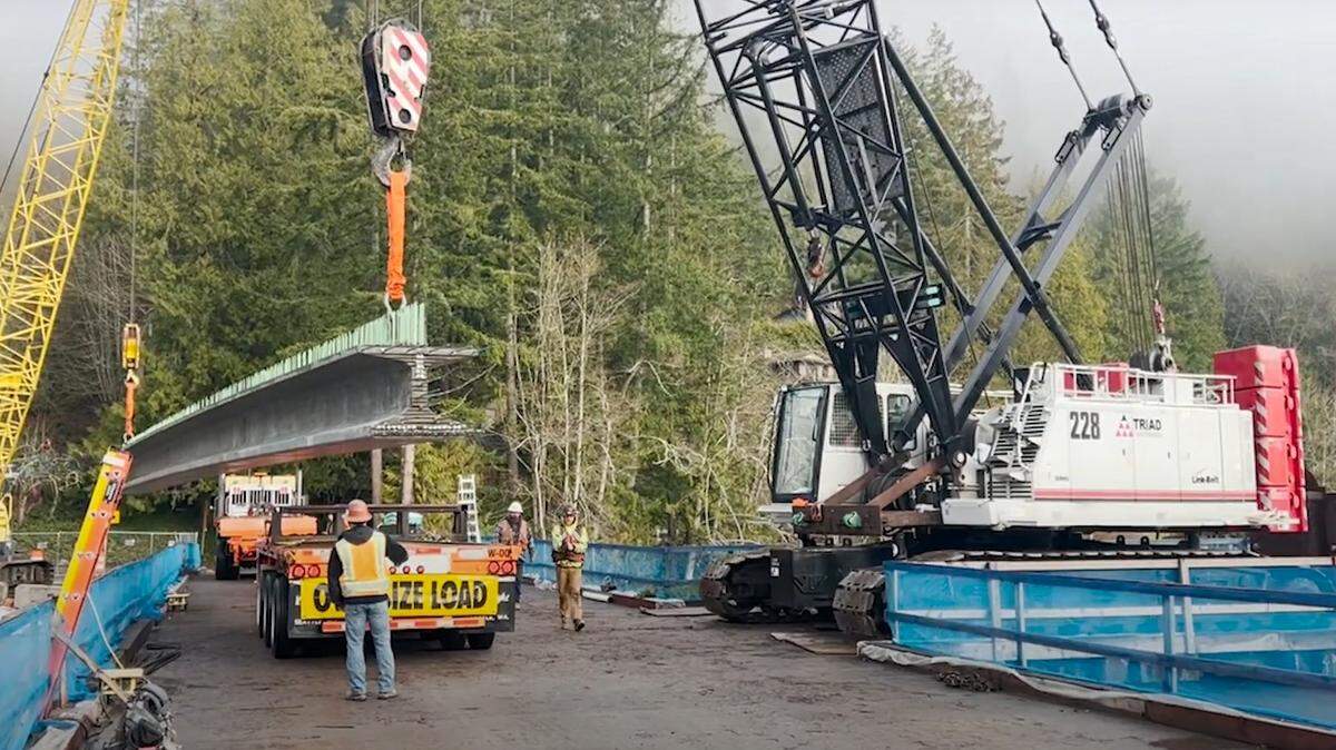 Construction workers place a girder that is 90 feet long and weighs almost 70,000 pounds on the deck of the new Lake Samish bridge, in a screen grab from a January 2025 video outlining the work.