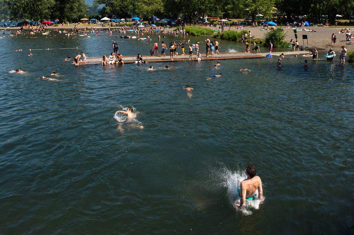 Teens jump off the Electric Avenue bridge into the cool waters of Lake Whatcom as hundreds pack the area to combat the record heat at Bloedel Donovan Park on Sunday afternoon, June 27, in Bellingham.