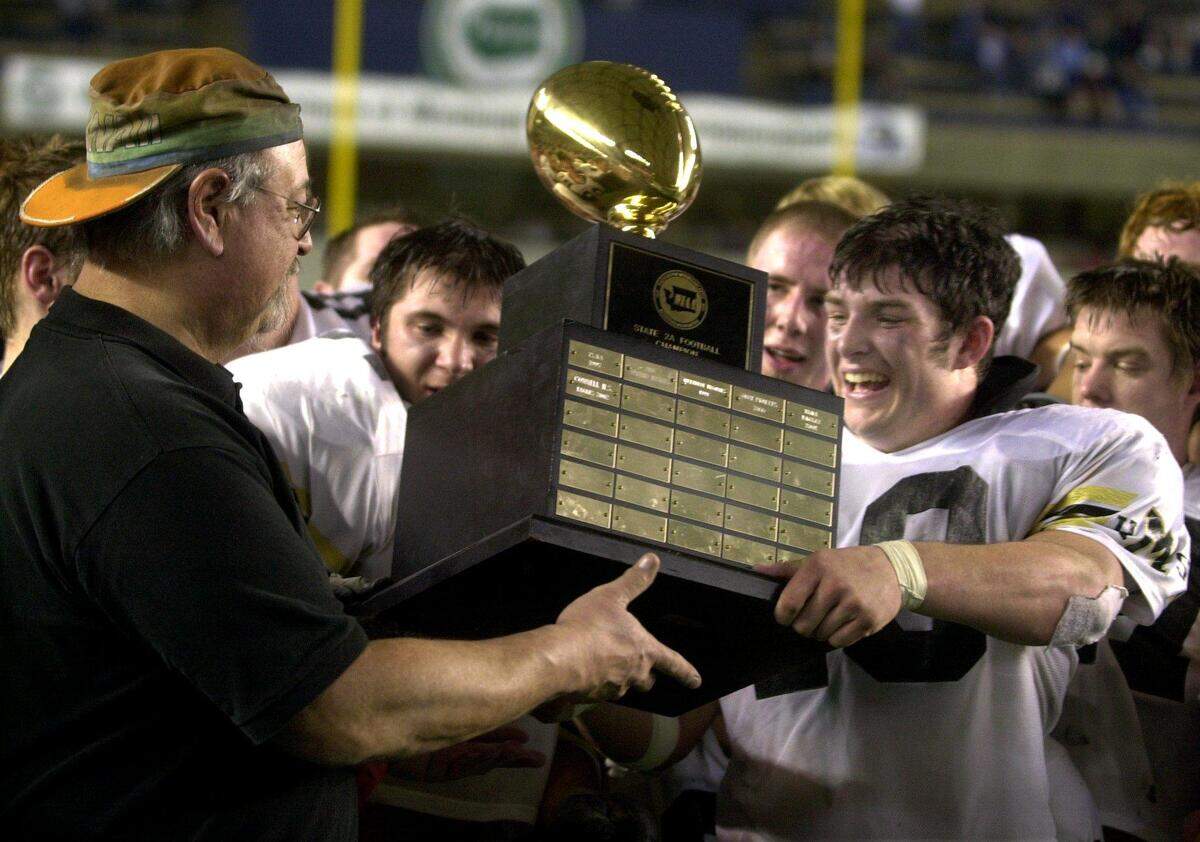 Meridian football head coach Bob Ames and running back/linebacker Brady Emmons hold up the trophy after the Trojans beat the Pullman Greyhounds, 34-10, to capture the 2003 Class 2A state football championship Saturday, Dec. 6, 2003, at the Tacoma Dome.