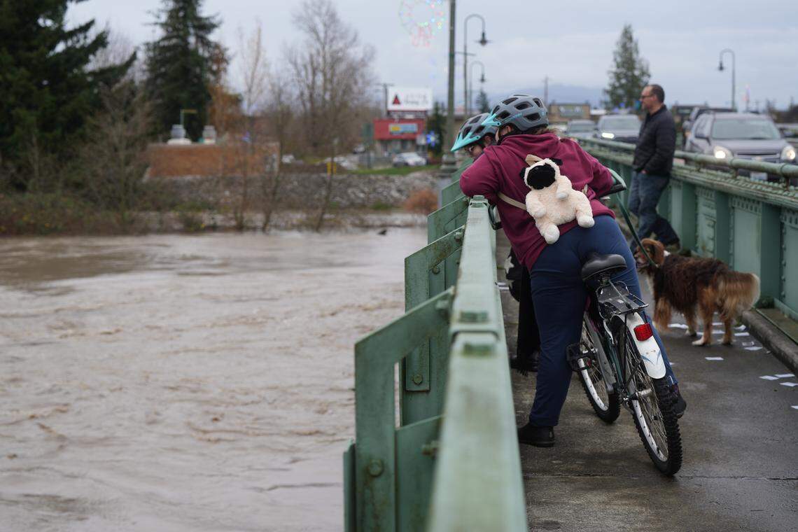 Pedestrians watch from Main Street Bridge as the Nooksack River flows quickly underneath on December 10, 2025, in Ferndale, Wash.
