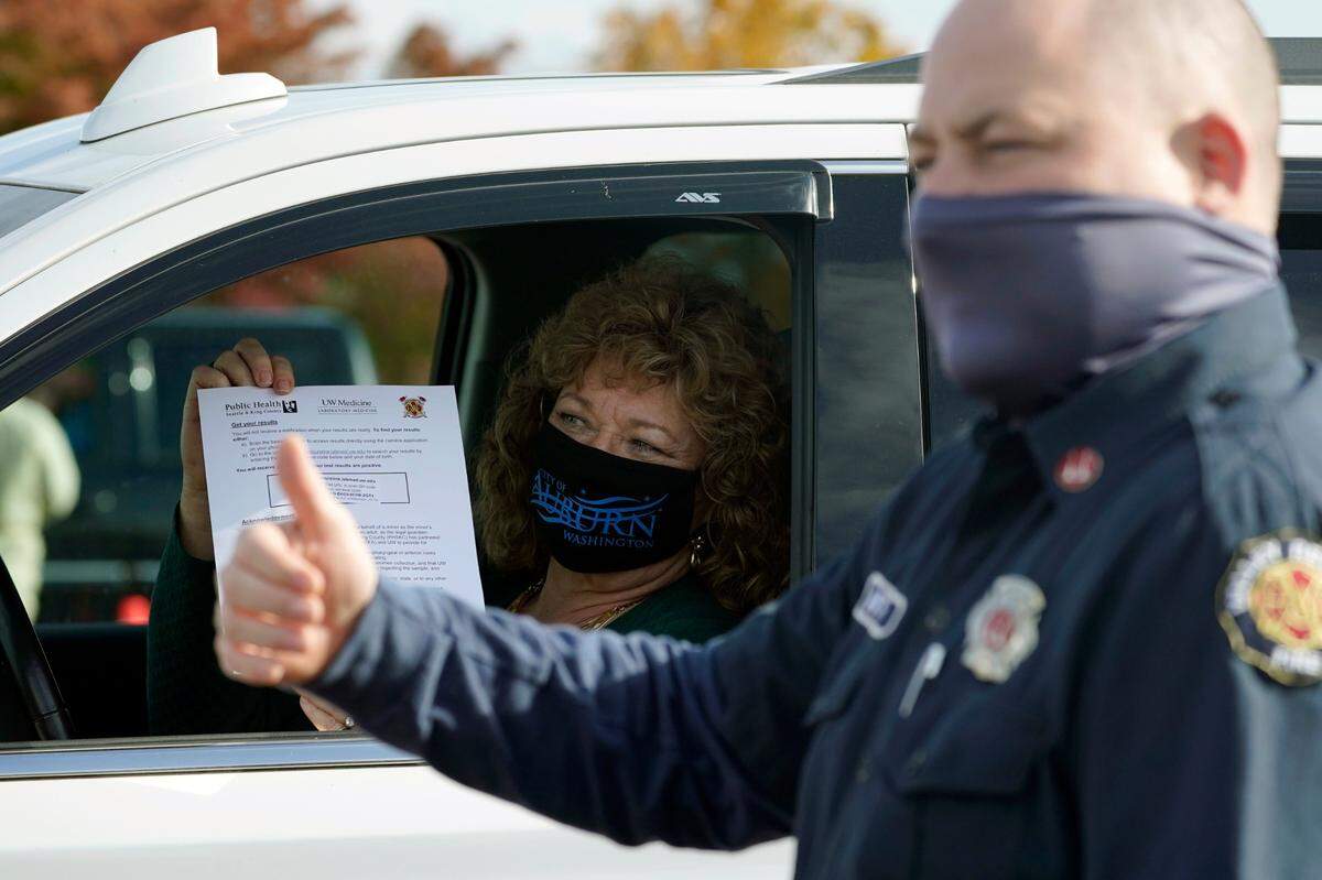 Nancy Backus, left, the mayor of Auburn, gets a thumbs-up from a firefighter as she displays the form with instructions on how to retrieve the results of her COVID-19 test, after she was tested at a King County COVID-19 testing site in Auburn Wednesday, Oct. 28. State health officials say that a new COVID-19 report released Wednesday shows an increase in coronavirus cases and hospitalizations throughout Washington state, and if not brought under control, officials said the spike could jeopardize progress toward reopening schools, strain the health care system and increase risks during the holiday season.