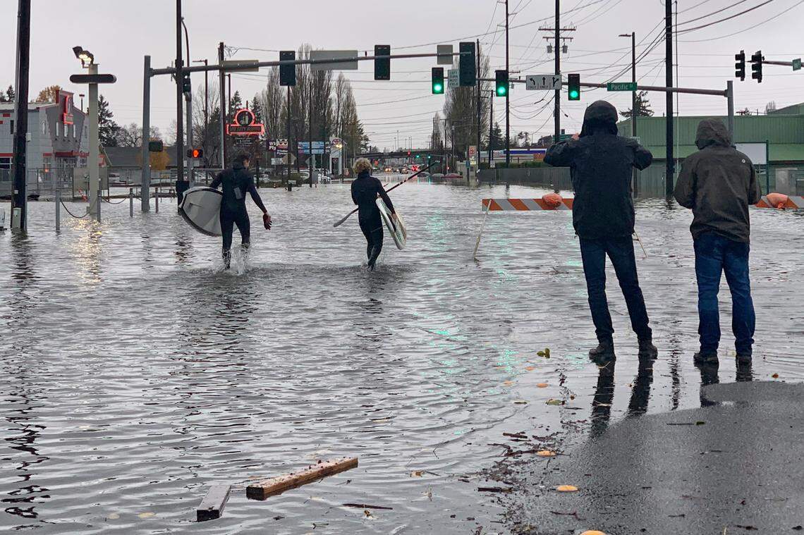 Caylon Coomes, second from left, and another man prepare to paddleboard in floodwaters on city streets in Bellingham Monday, Nov. 15. Widespread flooding in the Pacific Northwest amid days of heavy rainfall caused people to evacuate their homes, stranded drivers, and closed businesses, roads and schools.