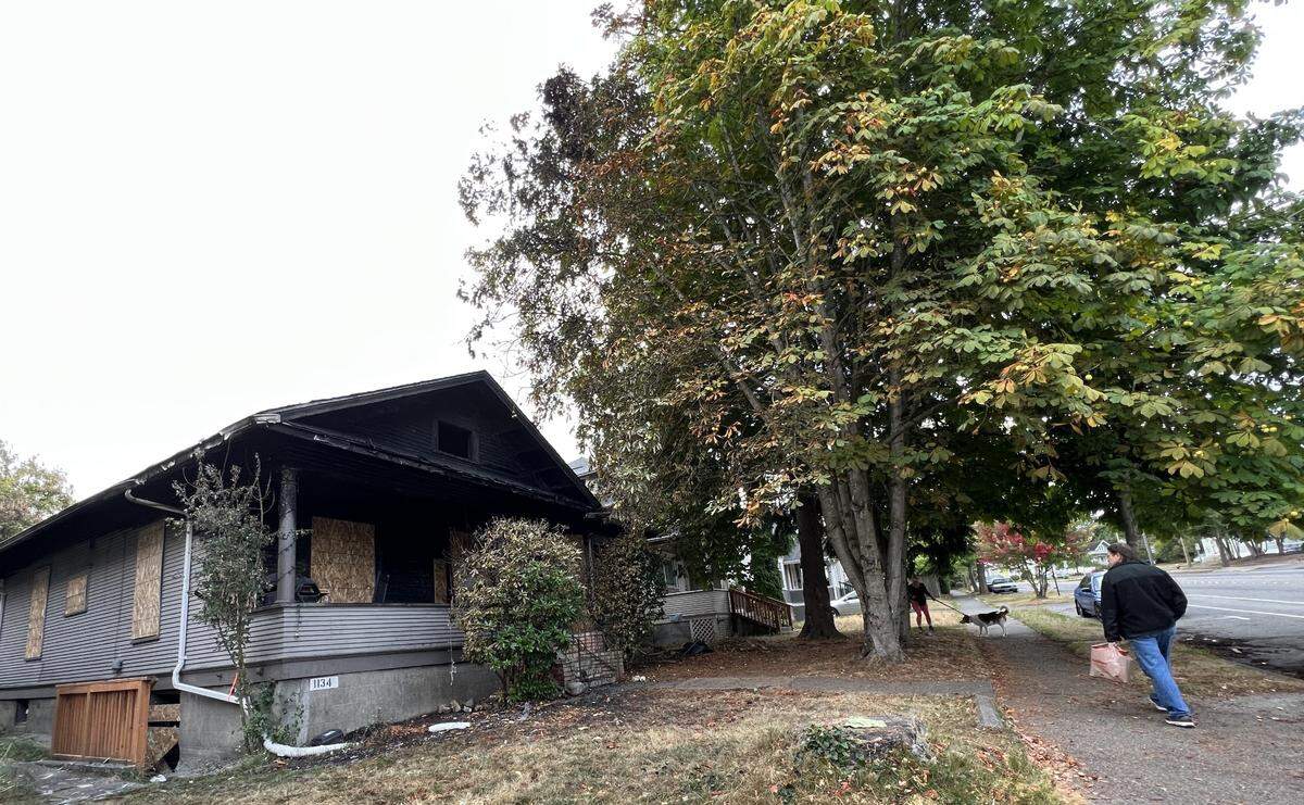 A man walks past a boarded-up house at 1134 Ellis St. in Bellingham, Wash., on Monday, Sept. 18, 2023, where a 7 a.m. fire the before injured one person, Bellingham Fire Department officials said.