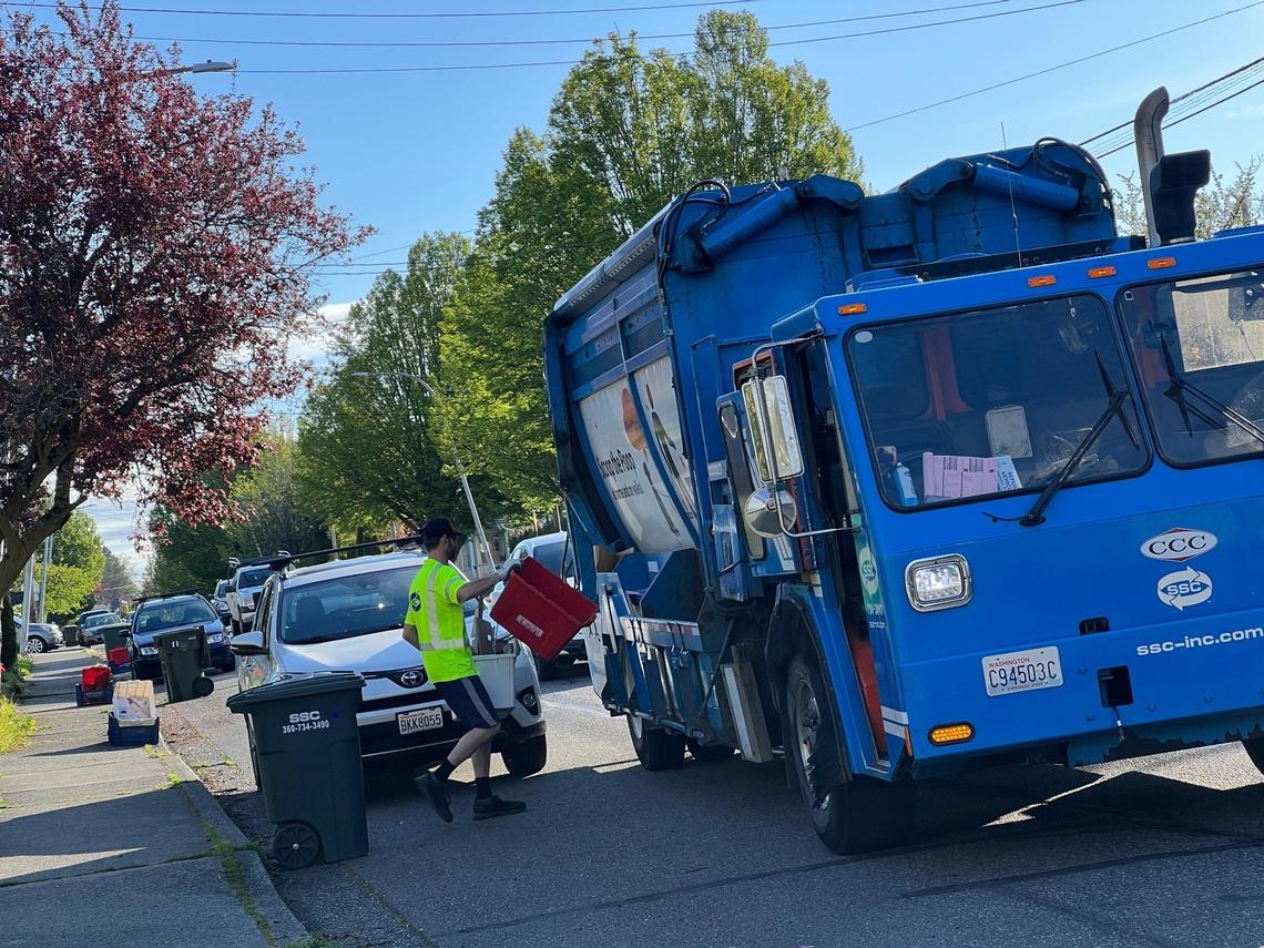 A worker for Sanitary Service Co. empties recycling bins into a truck on F Street near Halleck Street on Tuesday, May 9, 2023, in Bellingham, Wash. New single-bin recycling containers can be loaded onto trucks with mechanical arms, and reduce injuries among drivers who currently must leave the truck to lift and empty the bins themselves.