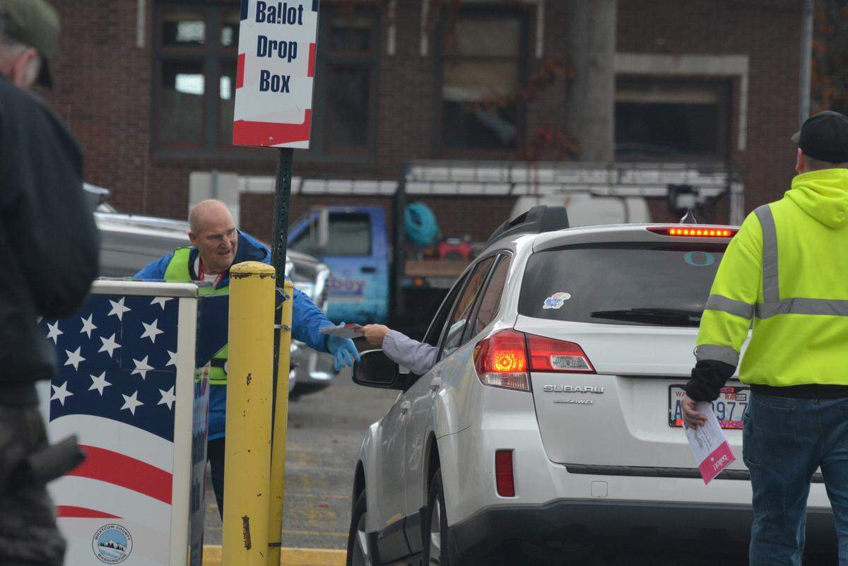 An election worker who is emptying a ballot drop box takes a ballot from a motorist as voters on foot and on bicycle wait in line to place their ballots in a drop box outside the Whatcom County Courthouse on Election Day.
