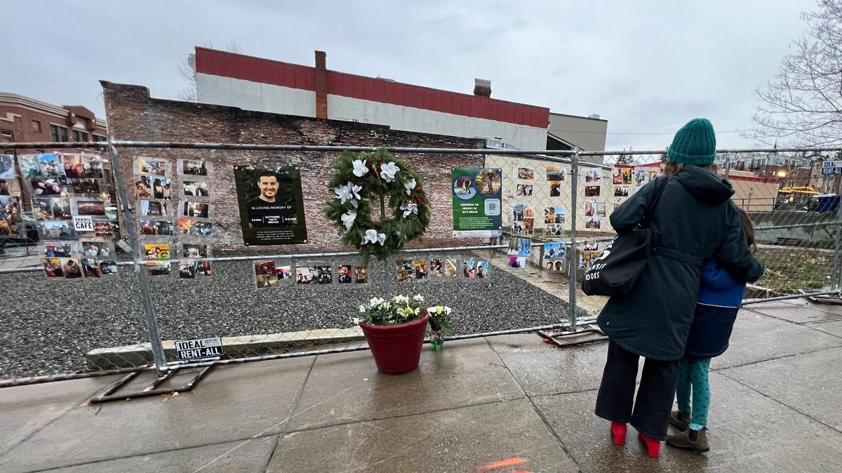 A mother and child pause in the rain Friday, Dec. 13, on Harris Avenue near 11th Street in the Fairhaven district of Bellingham, where family and friends have set up a memorial to Nathaniel “Nate” Breaux, who died in a fire at the Harris Avenue Cafe on Dec. 16, 2023.