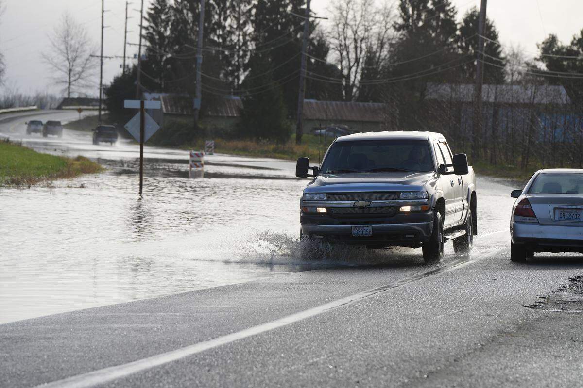 A motorist drives around road closure signs through water covering Hannegan Road on December 9, 2025, near Lynden, Wash.