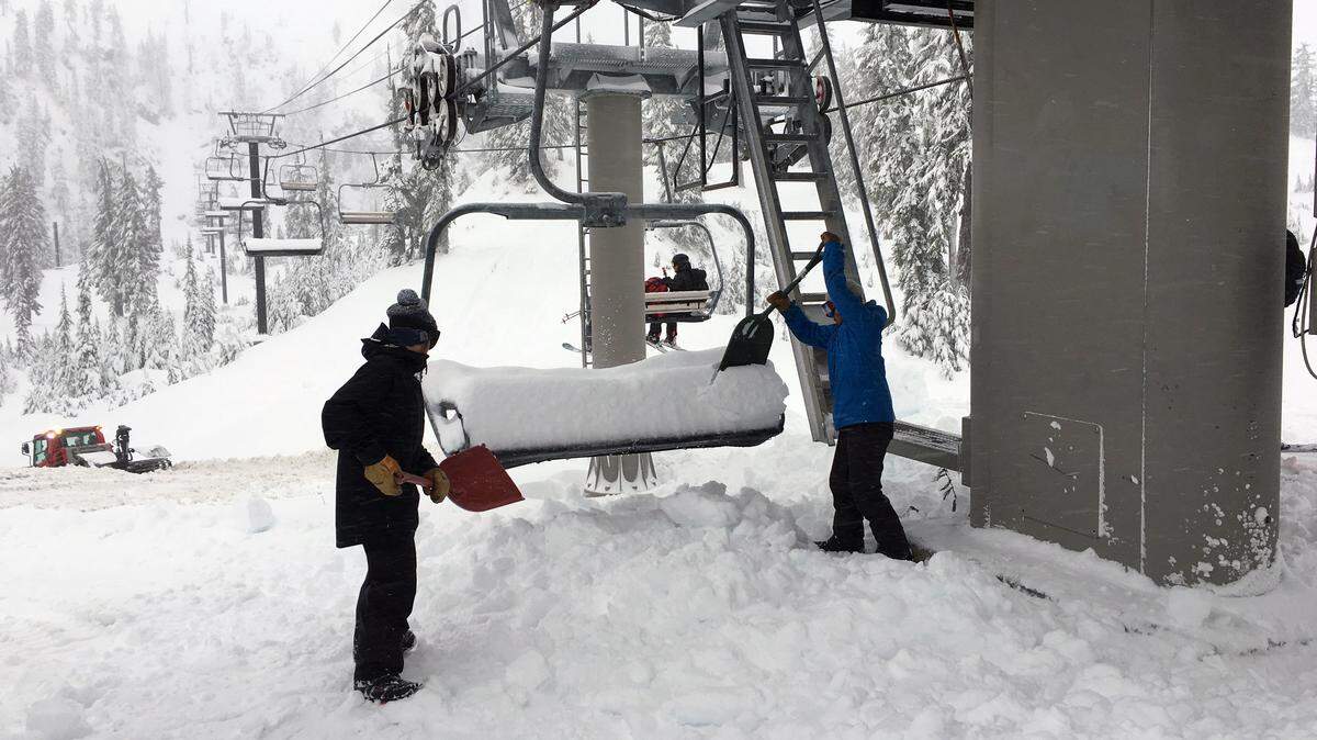 Crew members clean snow off Chair 1 at Mt. Baker Ski Area while Pro Patrollers ride the chair to set up boundary lines and signage on the mountain in 2017.
