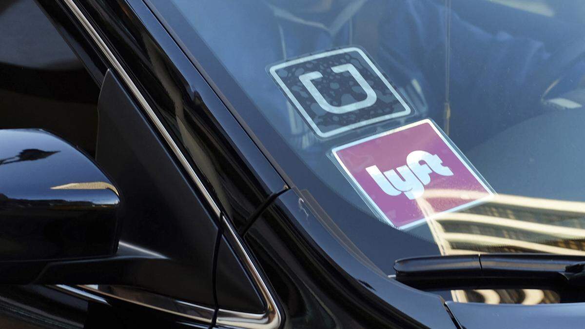 A ride share car displays Lyft and Uber stickers on its front windshield.