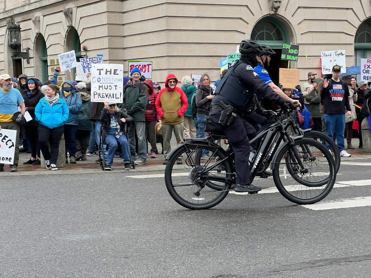 Bellingham Police officers on bicycles ride past anti-Trump protesters at the corner of Magnolia Street and Cornwall Avenue in downtown Bellingham, Wash., on March 4, 2025.