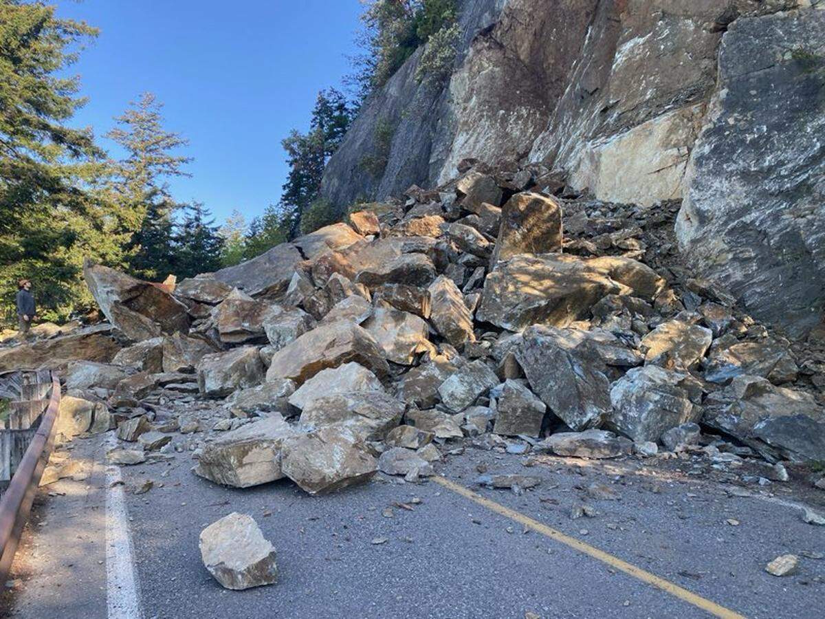 A person (left) looks up at a rockslide covering all lanes on Chuckanut Drive in Skagit County just north of Blanchard Road on April 22, 2025.
