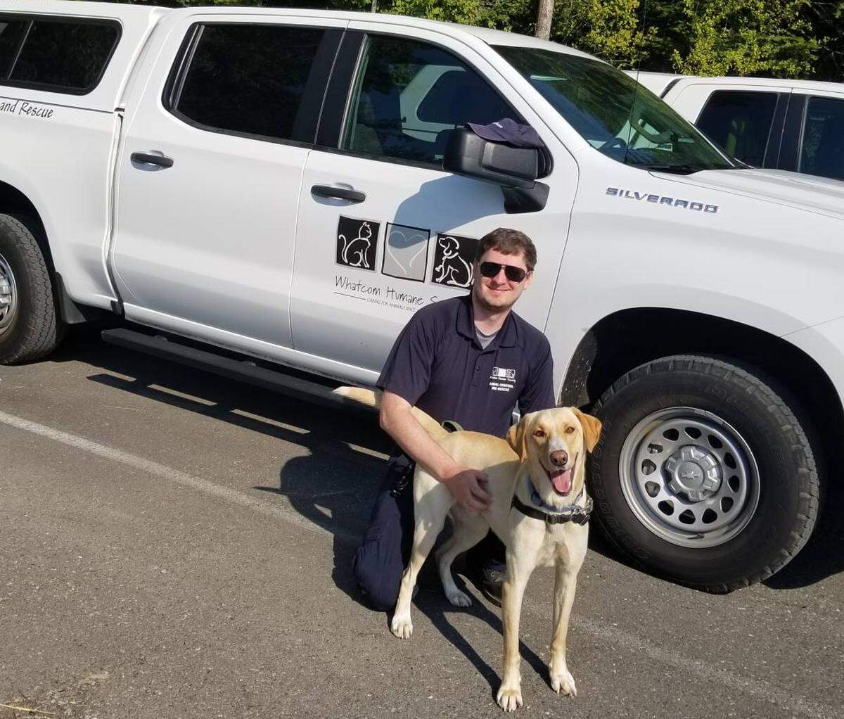 Animal control officer Kyle Berger poses in front of his vehicle with a dog.