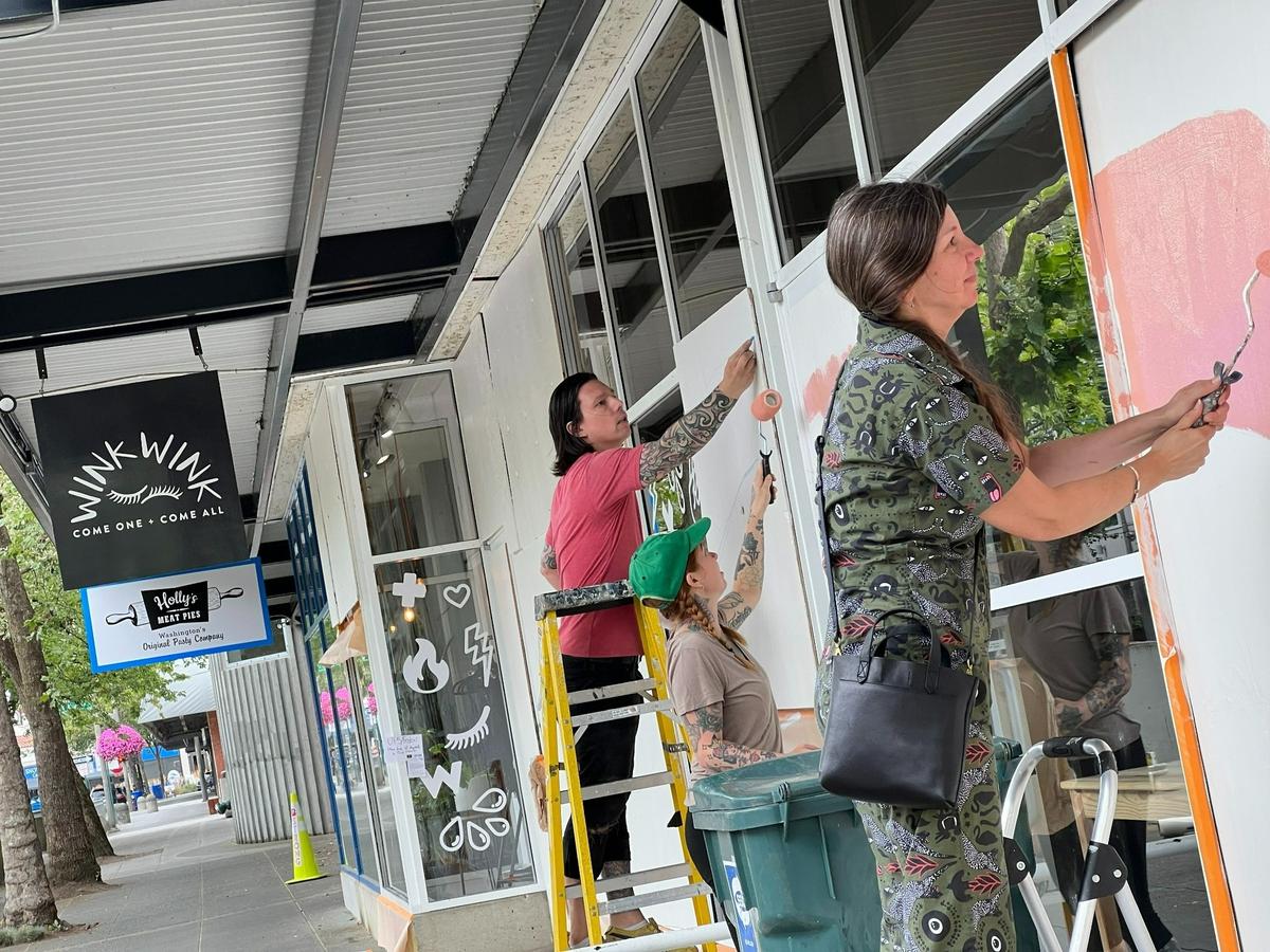 Volunteers Keith Negley, left, Jes Bonin and Heather Malcolm paint a mural on plywood that covers the shattered windows of Wink Wink Boutique in downtown Bellingham on Tuesday, Aug. 9.