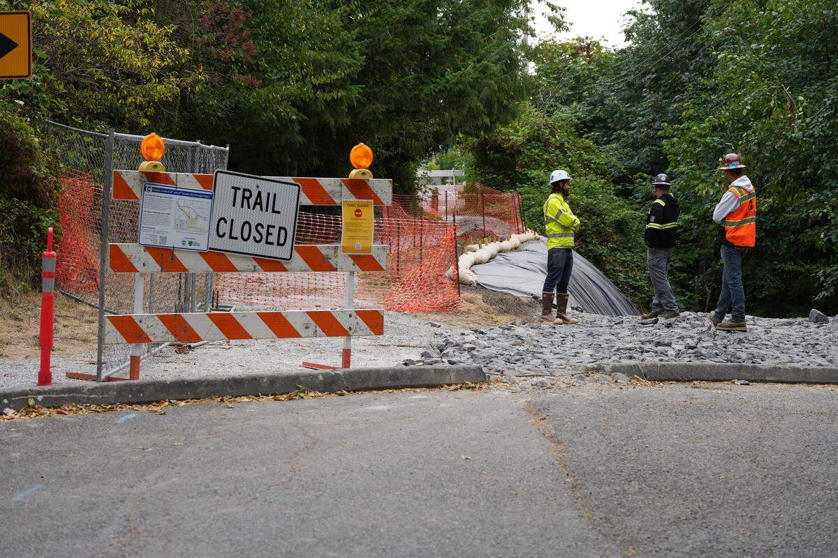 Employees with the Department of Ecology and the city of Bellingham stand next to a trail closure sign at the 10th Street entrance to the Interurban Trail on Wednesday in Bellingham. The trail was initially closed for a project to improve fish passage construction in Padden Creek, but a diesel spill during the project delayed operations while crews prioritized mitigation.