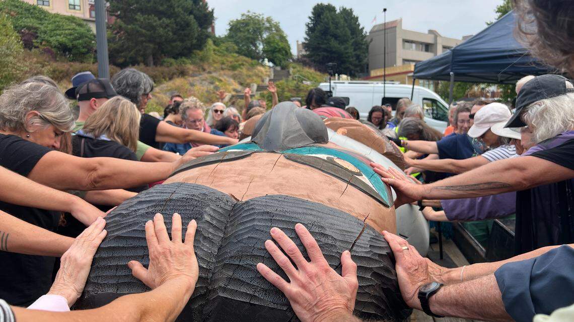 Those attending the Xaalh and the Way of the Masks ceremony lay their hands on a totem pole during a blessing led by The Rev. Dr. Jani Wild, rector of St. Paul’s Episcopal Church, on Saturday at Maritime Heritage Park in Bellingham.