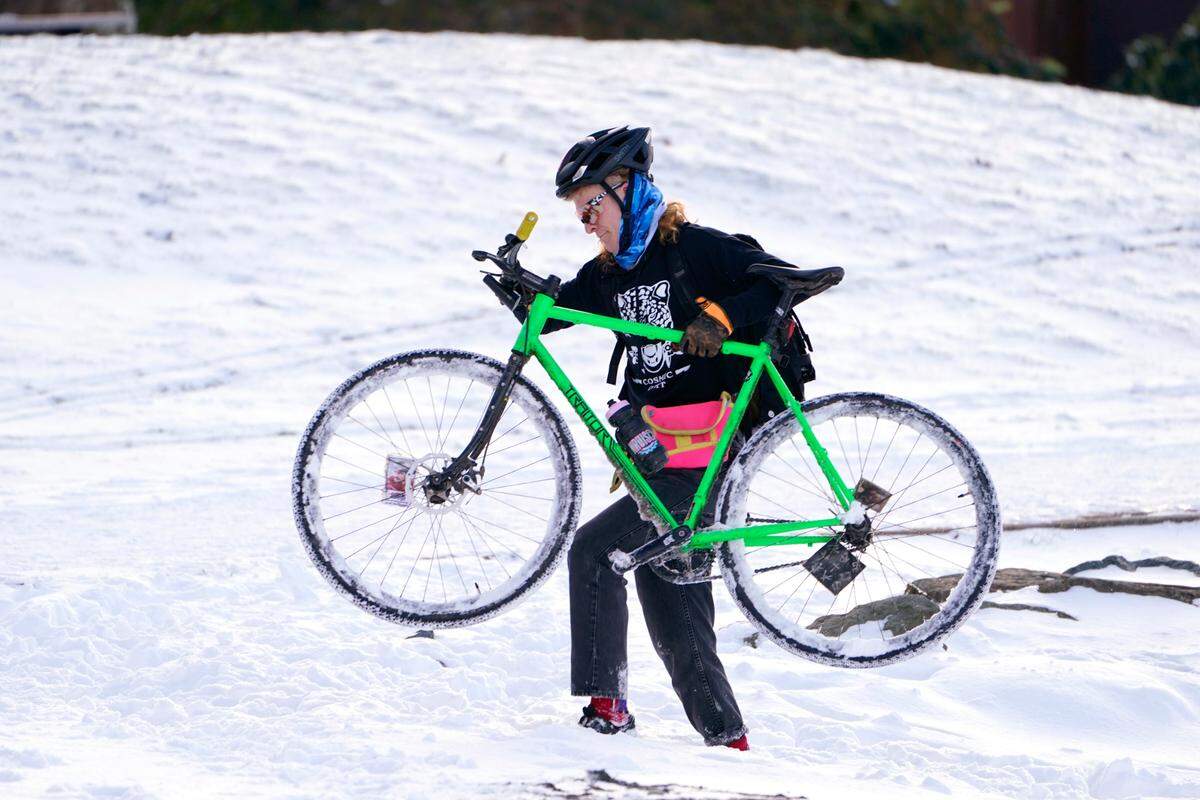 Apollo Leonard hefts his bike through snow too deep to ride in after stopping while out for a winter ride, Tuesday, Dec. 28, in Bellingham. Snow, ice and unseasonable cold in the Pacific Northwest continue to disrupt traffic, cause closures and force people to find refuge in emergency warming shelters.