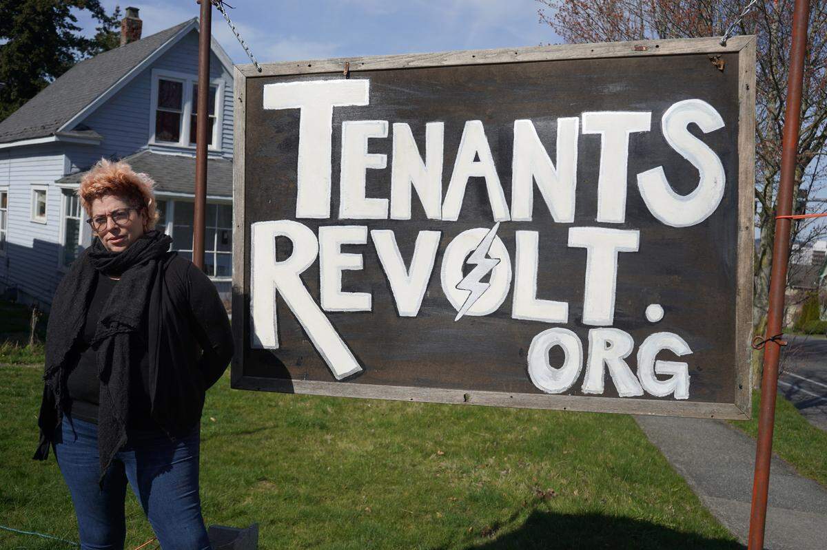 Rebecca Quirke of the renter advocacy group Tenants Revolt stands in front of her sign on the corner of Ellis Street and Potter Street on March 29, 2023, in Bellingham, Wash.