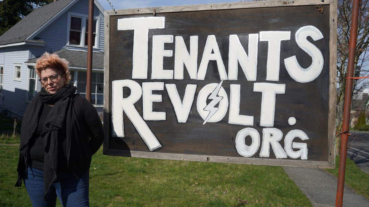 Rebecca Quirke of the renter advocacy group Tenants Revolt stands in front of her sign on the corner of Ellis Street and Potter Street on March 29, 2023, in Bellingham, Wash.