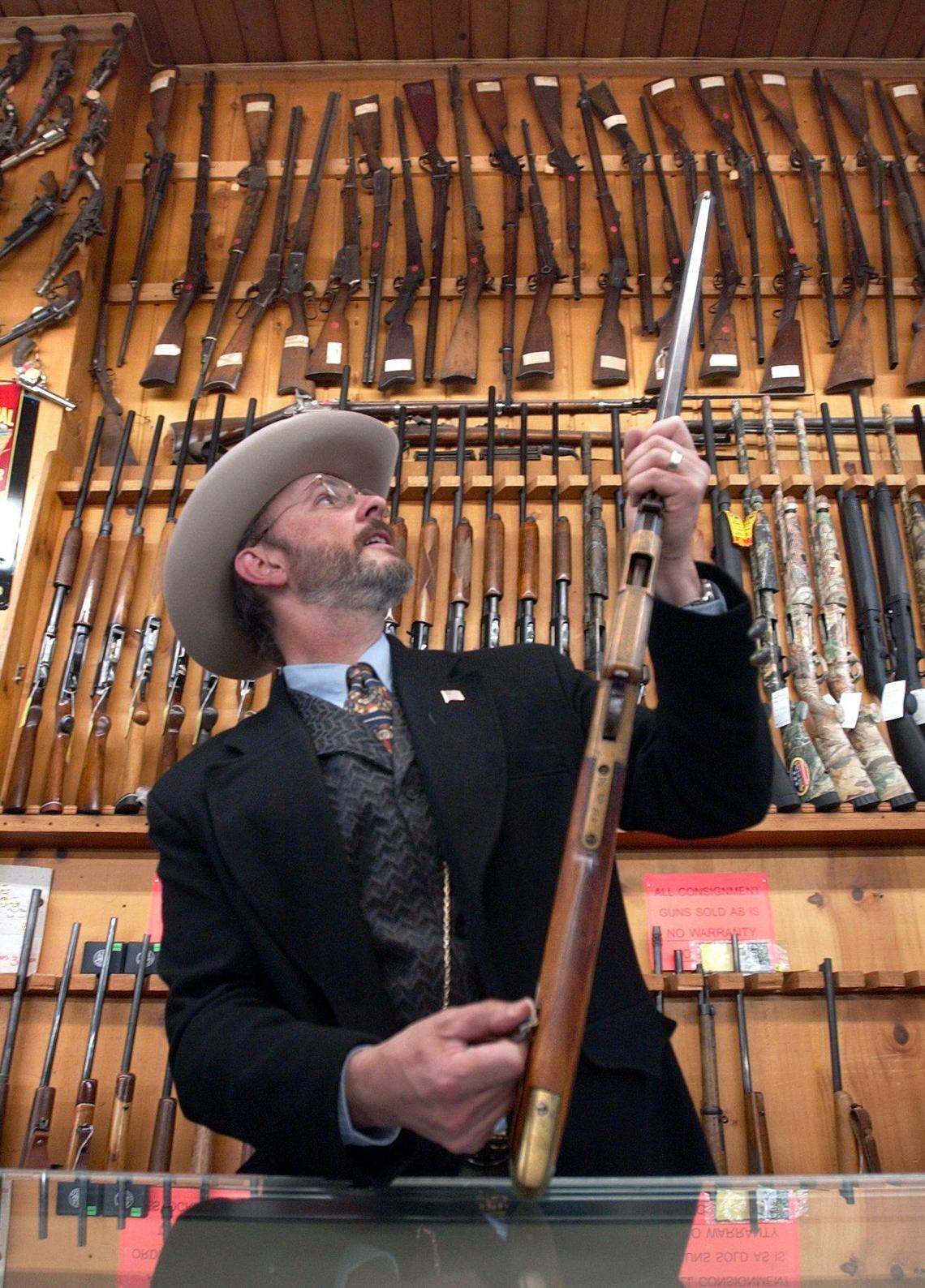 Ira Uhrig, wearing a white, '30s-style cowboy hat, boots, and with a pocket watch chain dangling from his vest, looks over a gun in the late Ira Yeager's collection of 471 antique guns that were auctioned off in 2003 after being displayed at Yeager's Sporting Goods, the family business.