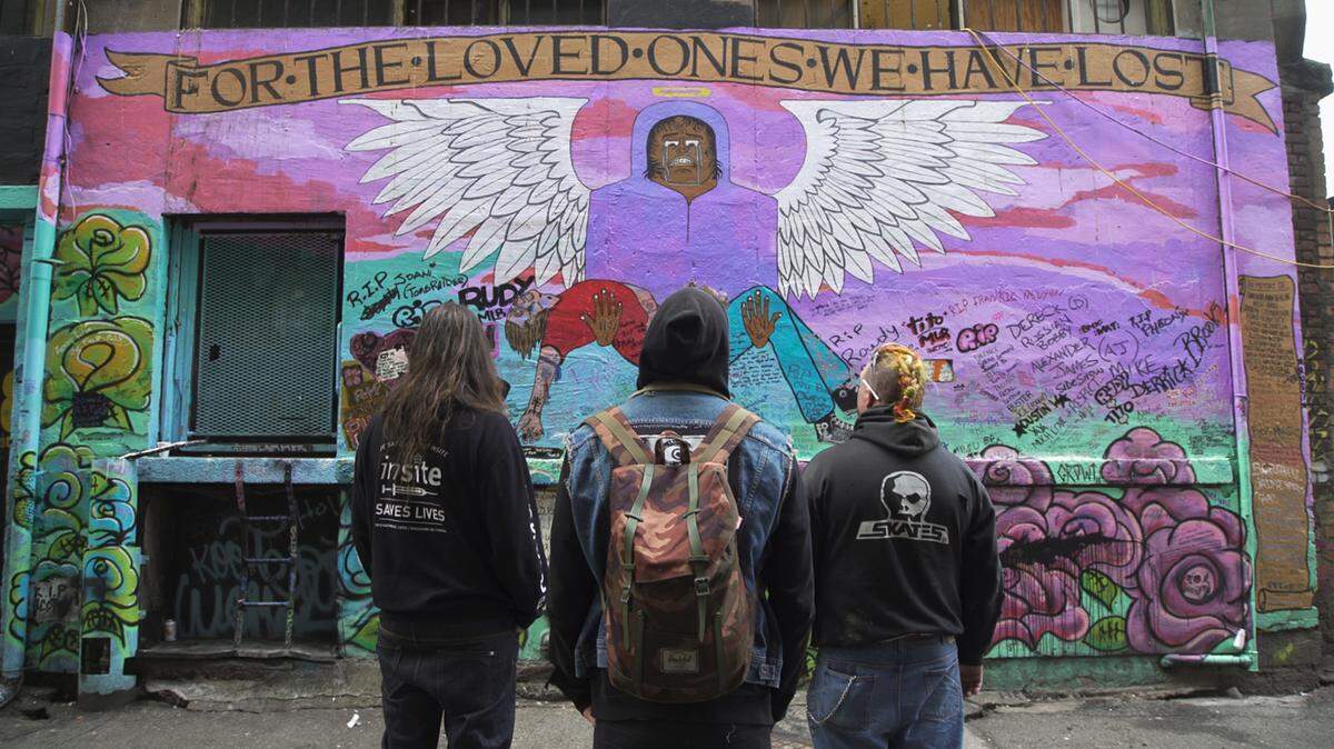 Ronnie Grigg, Trey Helton, and Shawn Hefele stand before a mural in the alley behind the Overdose Prevention Society created by Trey and Shawn as a memorial to overdose victims in the community.