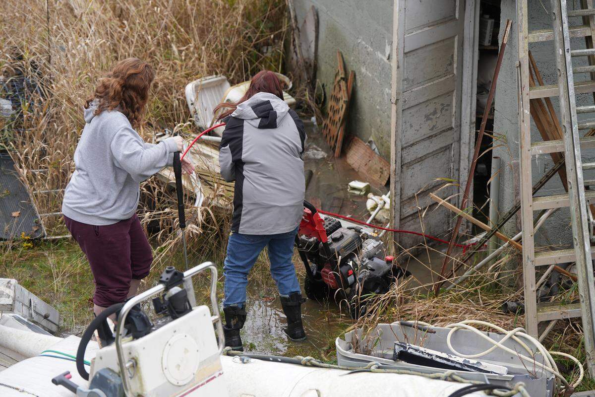 Makela Hatch (left) and Laura Buckley help clear valuable items out of Buckley’s brother’s garage in Ferndale, which was already completely flooded on December 11, 2025. Floodwaters were expected to continue to rise.