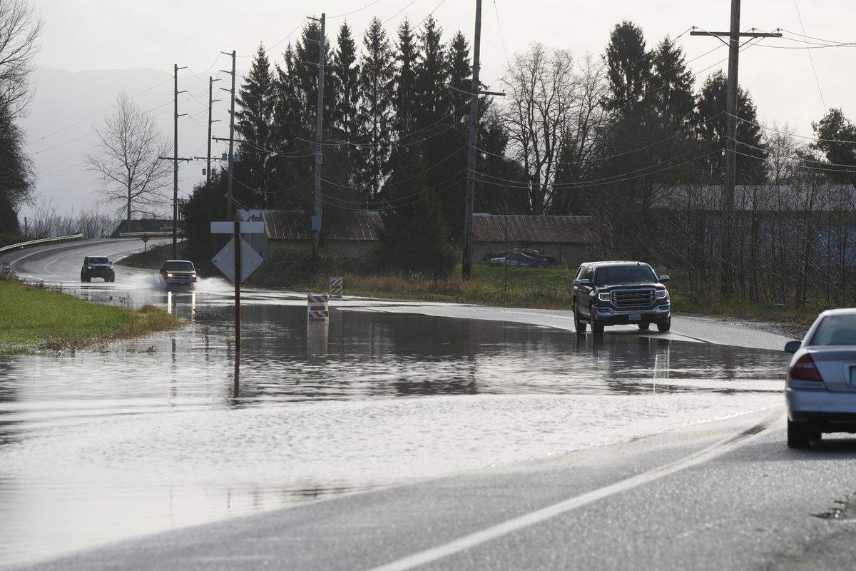 Motorists drive around road closure signs through water covering Hannegan Road on December 9, 2025, near Lynden, Wash.