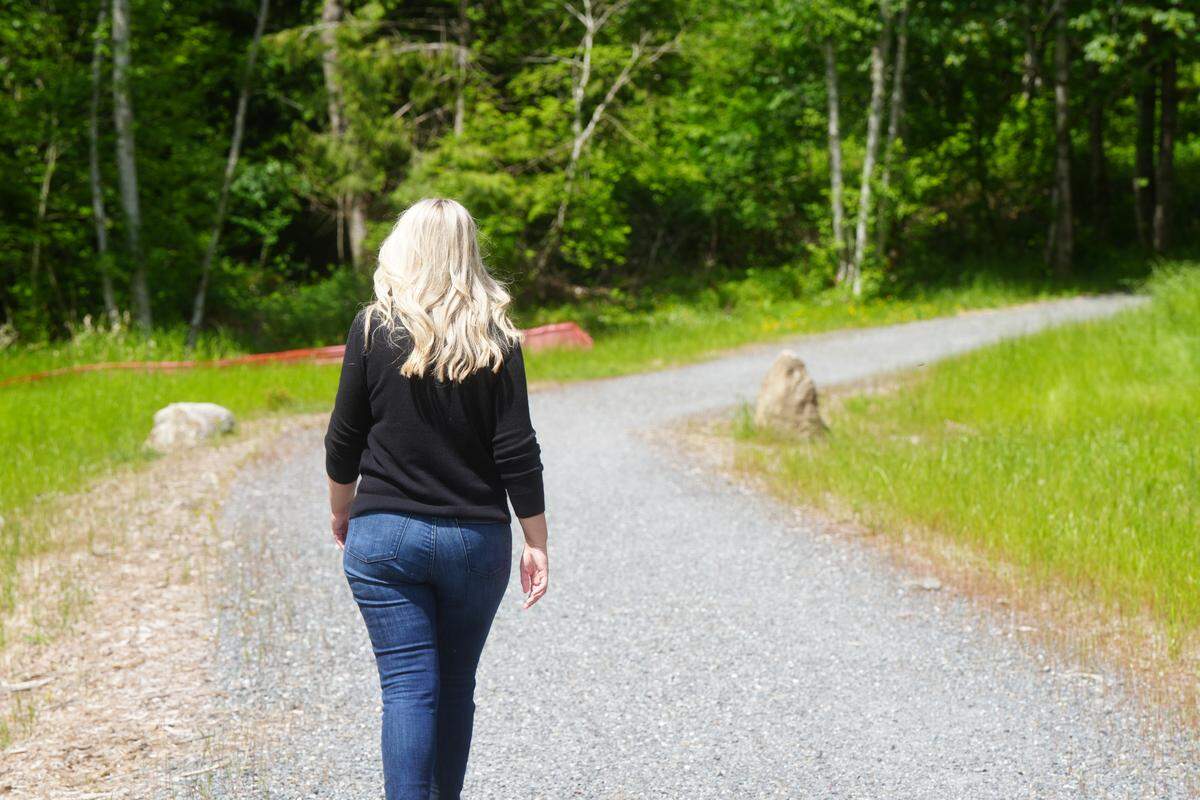 King Mountain homeowner Julie Jansen walks along a trail in her neighborhood on May 12, 2026. She said she frequently witnesses criminal activity on the trail related to the growing encampment on private property in the nearby woods.