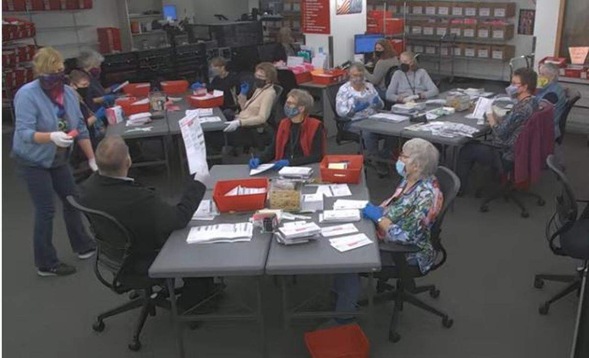 Workers in the Whatcom County auditor’s office election center, seen in a YouTube live stream image, process ballots Wednesday, Nov. 3, in Bellingham. They remove the security sleeve containing the ballot from the return envelope to inspect to ensure the votes marked will be read by the scanning equipment. Ballots needing additional adjudication or review are also flagged by these workers.