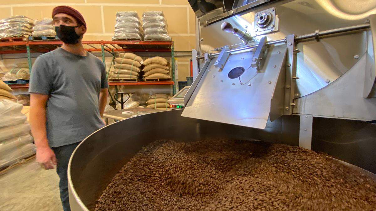 An employee at Tony’s Coffee stands next to a roaster while coffee beans are emptied on Thursday, Oct. 29, at Tony’s Coffee’s facility in Bellingham.