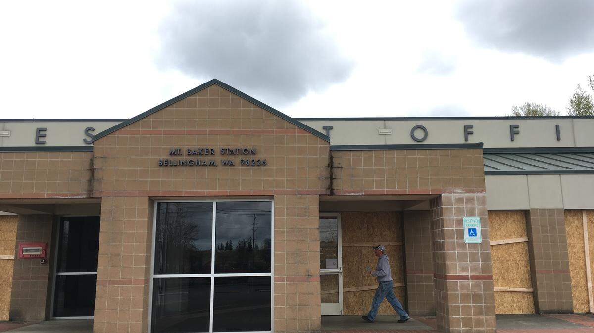 A Sunday patron walks past windows that are covered in plywood after the weekend vandalism at the post office's Mount Baker Station on Orleans Street in Bellingham.