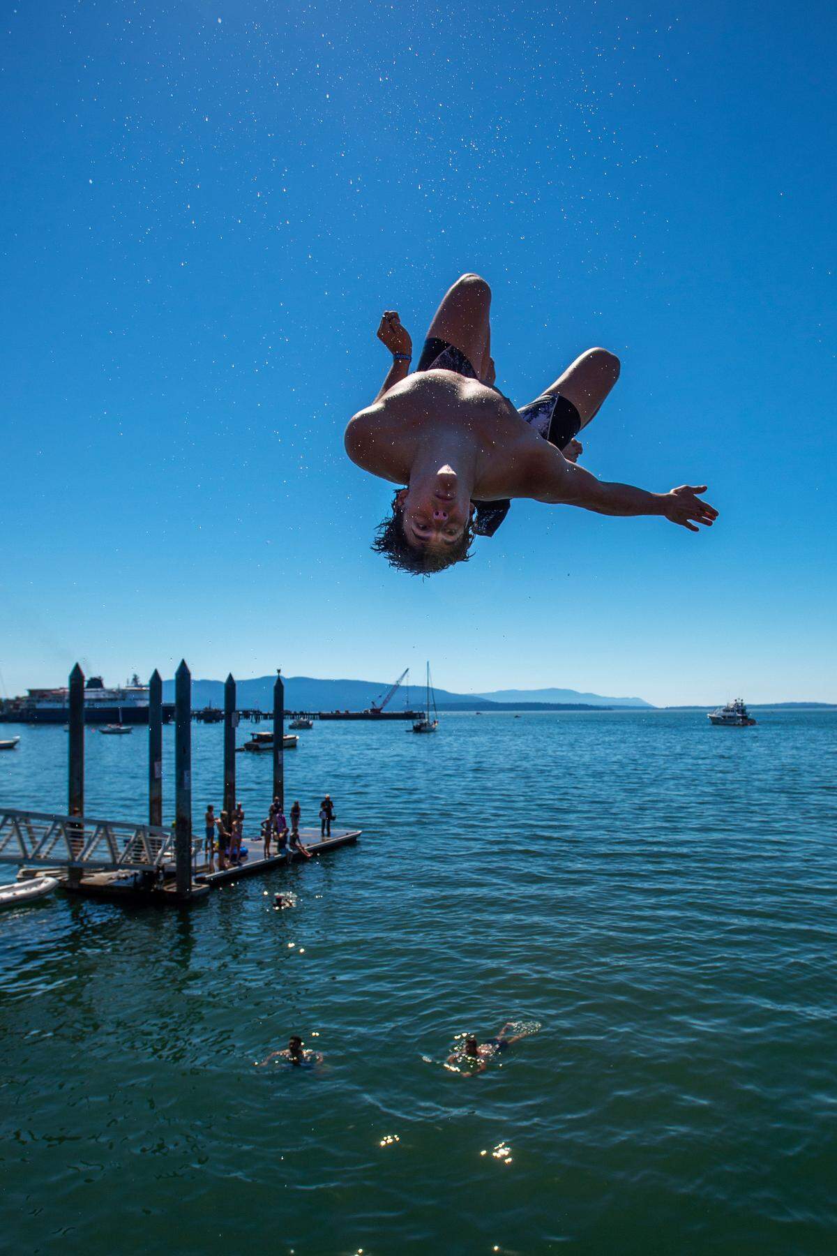 Western Washington University sophomore Nathan Parker of Bellingham performs a twisting back-flip off the Boardwalk at Taylor Dock in Boulevard Park in an attempt to escape the oppressive heat on Saturday afternoon June 26, in Bellingham.