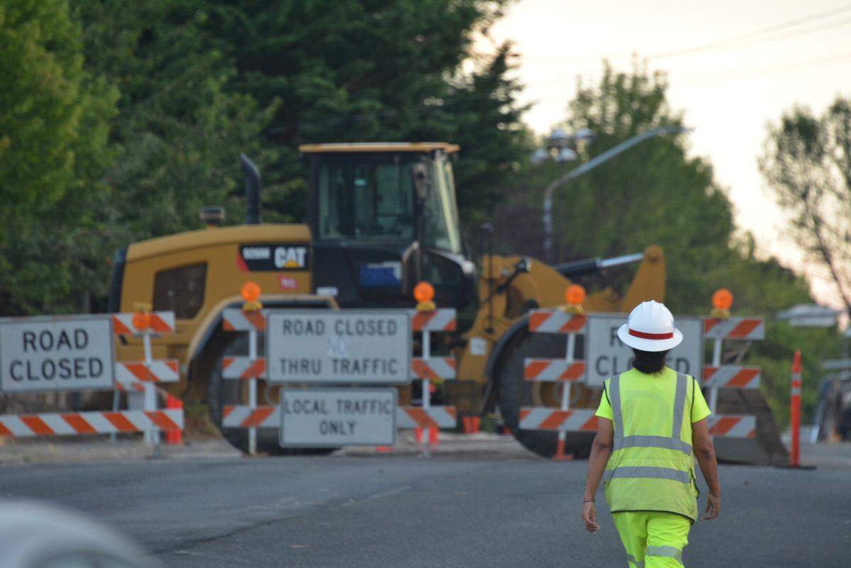 A construction worker walks past road closure signs on Woburn Street near East Illinois Street on Thursday, Aug. 17, 2023, in Bellingham, Wash.