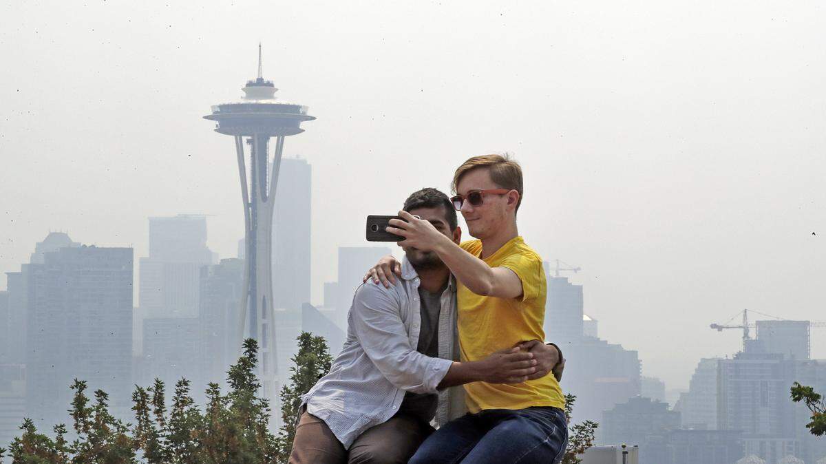 Adi Kang, left, and Brendon Walter take a photo together as a smoky haze obscures the Space Needle and downtown Seattle behind them, Tuesday, Aug. 14, 2018. Public-health officials are warning of unhealthy air across parts of the Pacific Northwest as smoke from wildfires move across the region.
