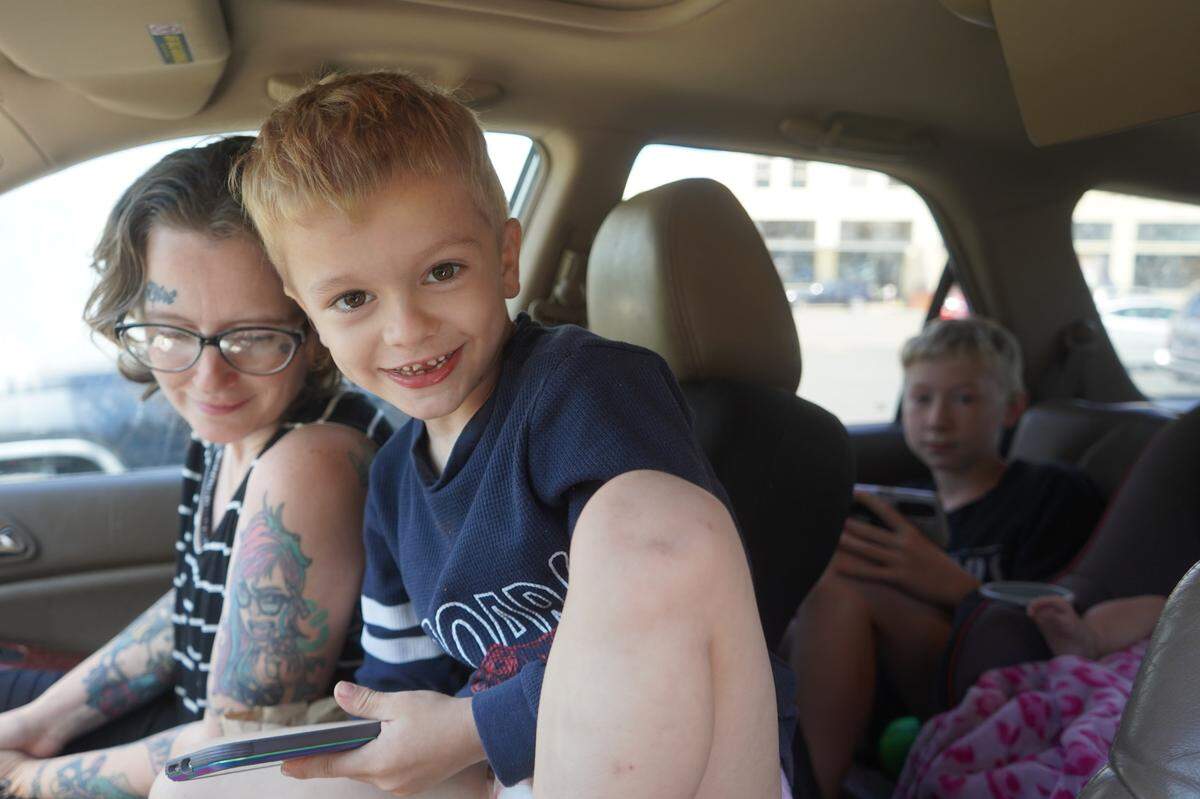 Cassandra sits with one of her six children in the front seat of their vehicle on July 27, 2023, in a parking lot in downtown Bellingham, Wash. Cassandra’s older son sits in the back seat next to her youngest daughter. The family of eight is living in the vehicle until they can get into supportive housing.