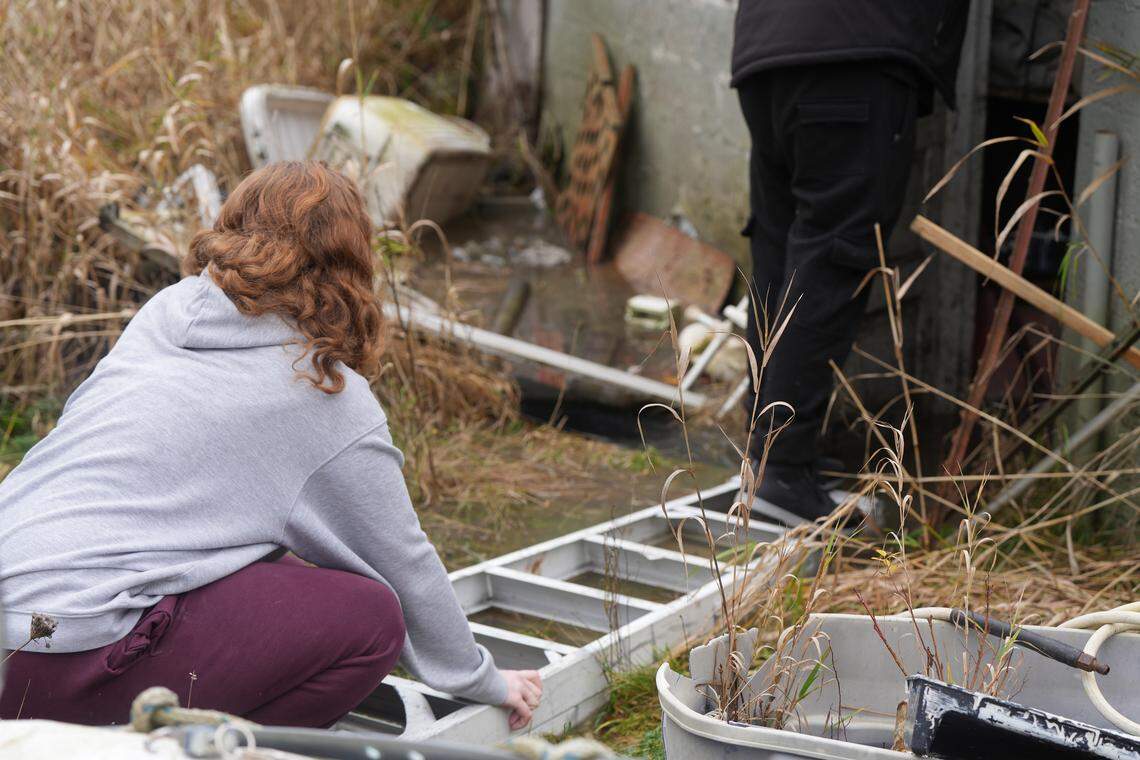 Makela Hatch (left) stabilizes a ladder over floodwaters to help her fiancé, Colton Moore, get inside his uncle’s garage in Ferndale, which was already completely flooded on December 11, 2025. Floodwaters were expected to continue to rise.