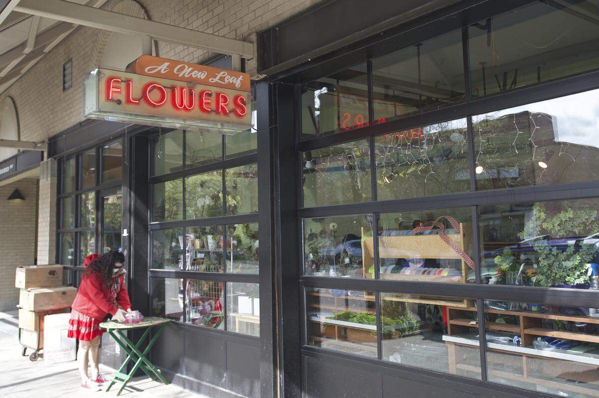 A masked customer picks up an order from A New Leaf Flower Shoppe Friday, May 1, in downtown Bellingham. Trisha Manley re-opened her shop April 22 for no-contact deliveries during the coronavirus pandemic, in time for Mother’s Day flower sales.