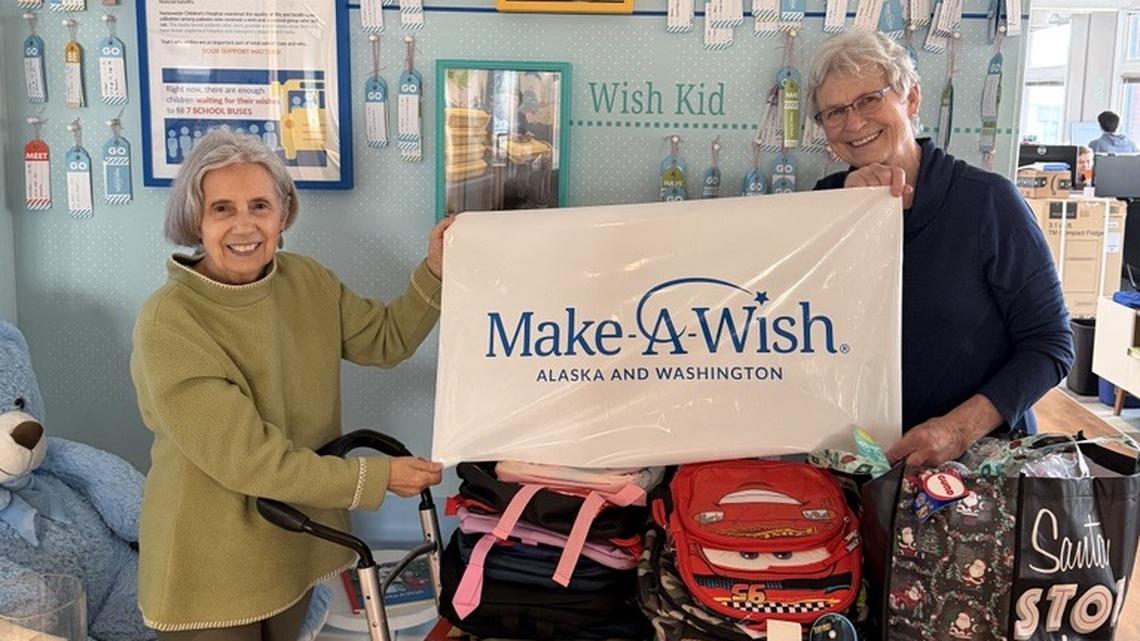 Charlotte Pollard (left) and Becky Wageman hold a Make-A-Wish Washington and Alaska banner. The nonprofit organization is celebrating its 40th year of the Washington and Alaska branch.