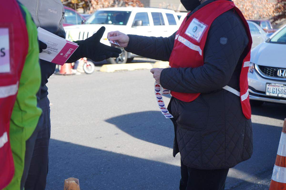 An election volunteer hands an “I voted” sticker to a voter dropping their ballot in an official drop box near the Whatcom County Courthouse on Election Day, Tuesday, Nov. 8, in Bellingham.