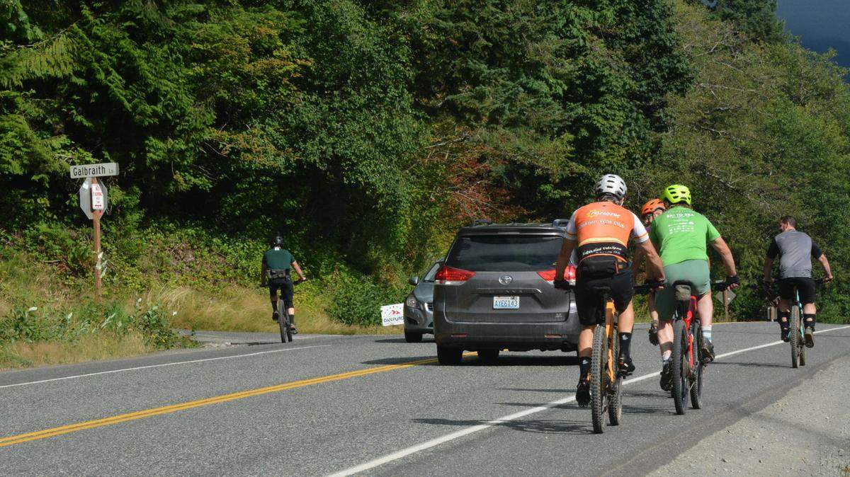 Mountain bikers on Samish Way head toward Galbraith Lane, which provides miles of trails on Wednesday, Aug, 9, 2023, outside Bellingham, Wash. Cars parked on the south side of the road often take up the shoulder and force bicyclists into traffic.