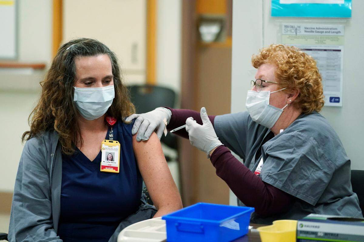 LaRae Munns, left, a nurse in the Emergency Department at Madigan Army Medical Center, receives one of the first doses of the Pfizer vaccine for COVID-19 from nurse Goldie Martin, right, Wednesday, Dec. 16, 2020, at Madigan Army Medical Center at Joint Base Lewis-McChord, south of Seattle.