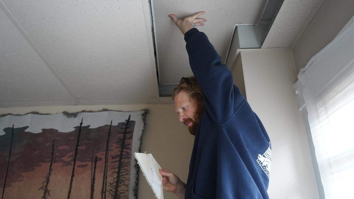 Aidan Hersh lifts up the drop ceiling in his rental unit at 1210 Ellis St. in 2023 in Bellingham. He holds a broken ceiling piece.                              